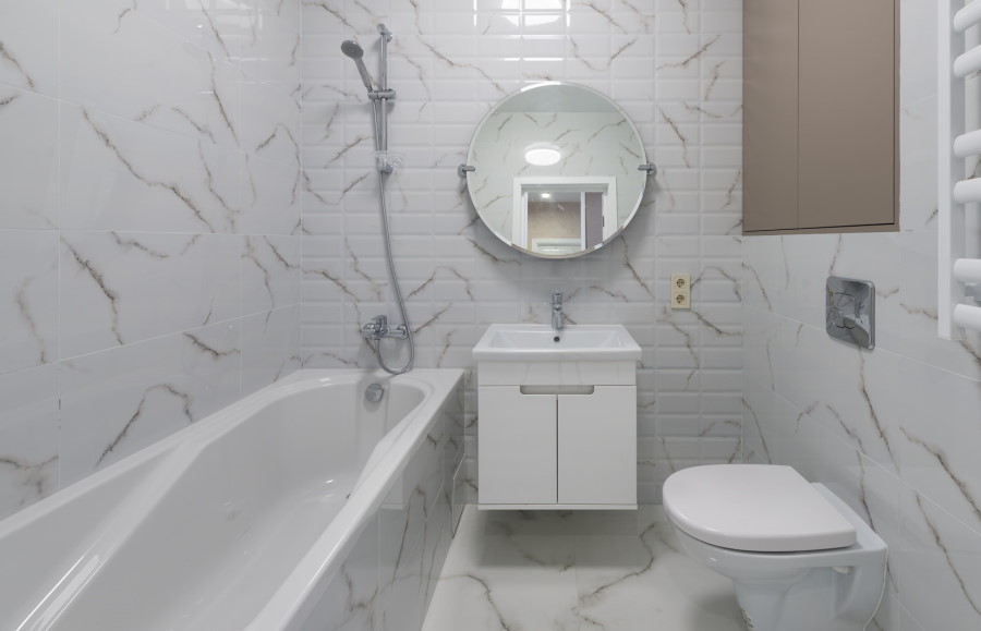Μικρός χώρος μπάνιου με ολόκληρη μπανιέρα, κρεμαστή λεκάνη και νιπτήρα με στρογγυλό καθρέφτη