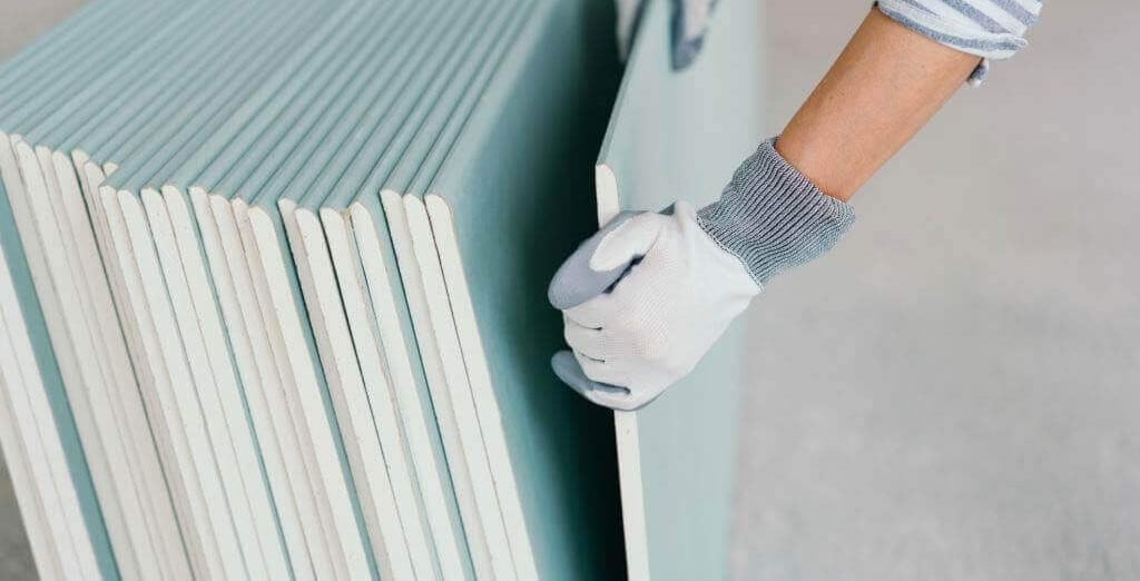 Φύλλα γυψοσανίδας σε στοίβα με ανδρικά χέρια να σηκώνουν ένα φύλλο γυψοσανίδας