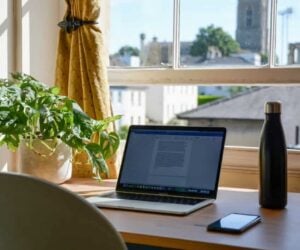Γραφείο στο σπίτι με φυτό και laptop μπροστά σε ένα παράθυρο