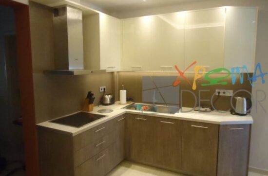 Ανακαίνιση κουζίνας στα Κάτω Πετράλωνα με γωνιακή διάταξη, λευκό πάγκο και ντουλάπια σε απόχρωση ξύλου