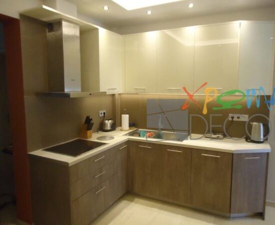 Ανακαίνιση κουζίνας στα Κάτω Πετράλωνα με γωνιακή διάταξη, λευκό πάγκο και ντουλάπια σε απόχρωση ξύλου