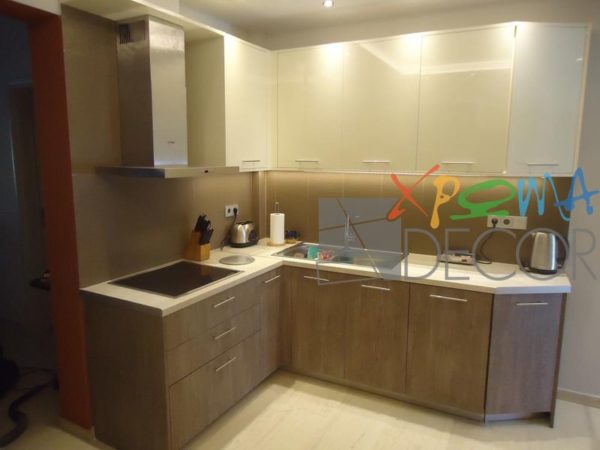 Ανακαίνιση κουζίνας στα Κάτω Πετράλωνα με γωνιακή διάταξη, λευκό πάγκο και ντουλάπια σε απόχρωση ξύλου