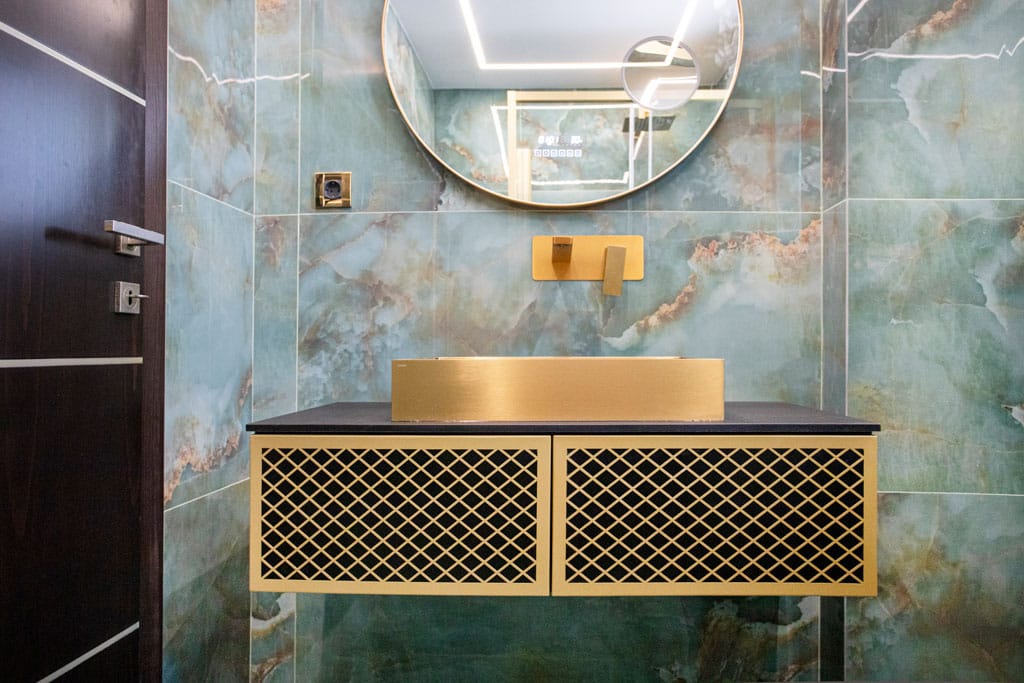 Νιπτήρας μπάνιου στα Πατήσια με χρυσή εντοιχισμένη μπαταρία, στρογγυλό καθρέφτη, έπιπλο με μεταλλική πρόσοψη και πλακίδια τύπου όνυχα