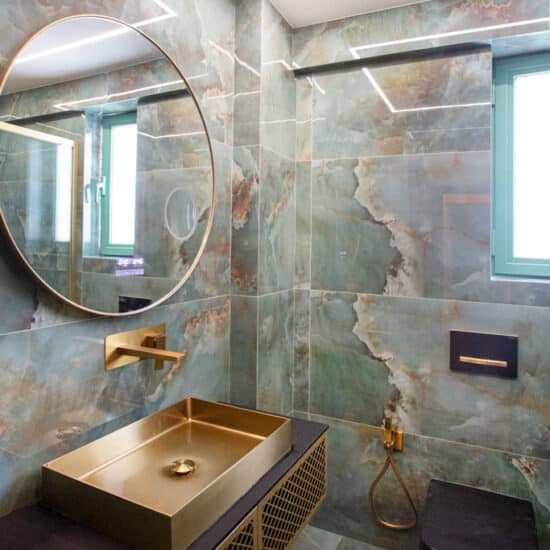 Μοντέρνο μπάνιο με πλακίδια τύπου όνυχα, χρυσό νιπτήρα, στρογγυλό καθρέφτη και εντοιχισμένο καζανάκι σε ανακαίνιση στα Πατήσια
