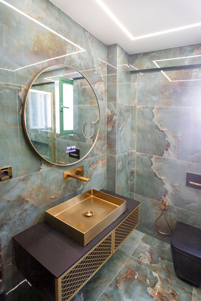 Ανακαίνιση μπάνιου στα Πατήσια με χρυσό νιπτήρα, επιτοίχια μπαταρία και στρογγυλό καθρέφτη