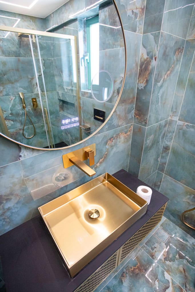 Χρυσός νιπτήρας με επιτοίχια μπαταρία και στρογγυλό καθρέφτη σε ανακαινισμένο μπάνιο στα Πατήσια με πλακίδια τύπου όνυχα