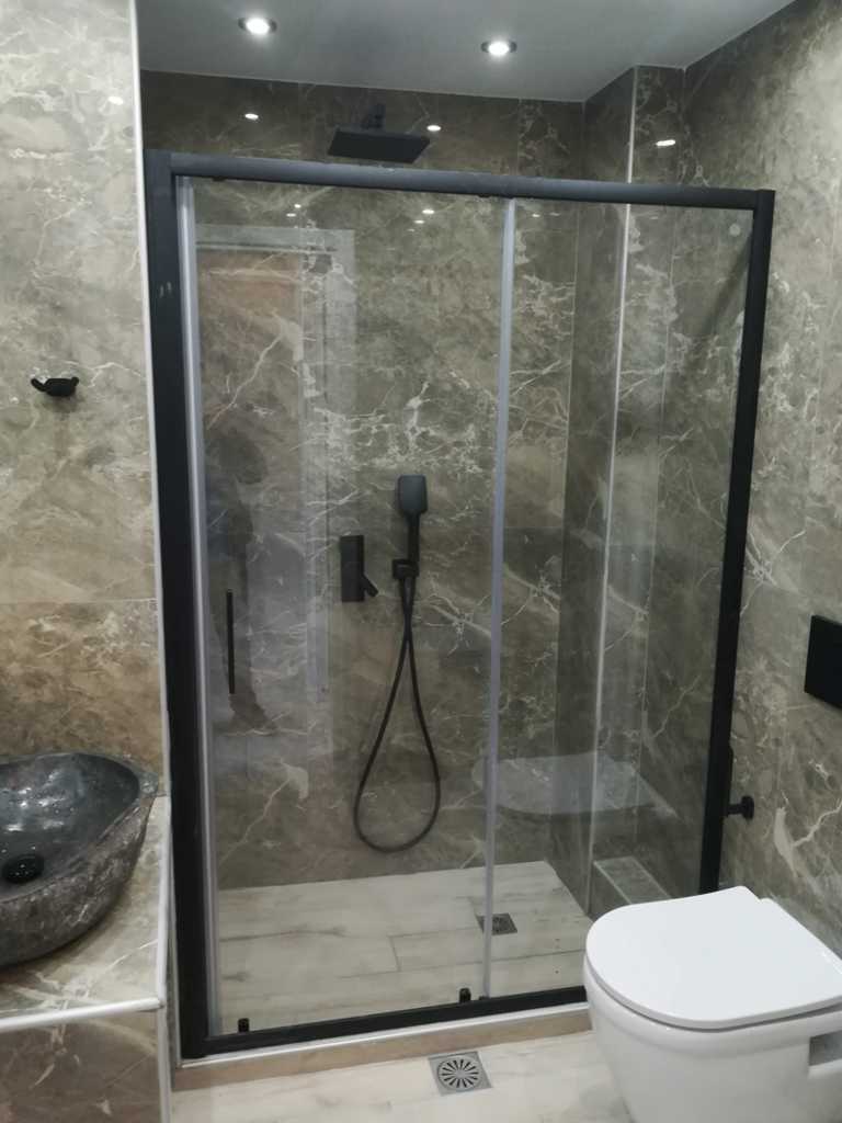 Σύγχρονο μπάνιο με μαύρη καμπίνα ντουζιέρας και πλακάκια μαρμάρινης υφής σε ανακαίνιση μπάνιου στον Ταύρο από τη Chroma Decor