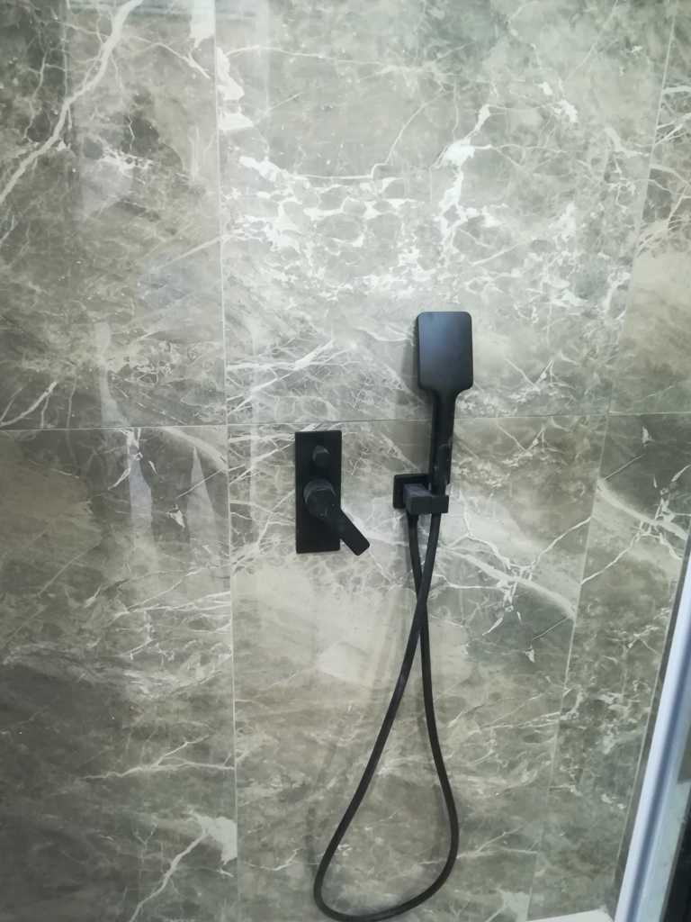 Μαύρη εντοιχισμένη μπαταρία ντους με τηλέφωνο σε τοίχο με πλακάκια μαρμάρινης υφής σε ανακαίνιση μπάνιου στον Ταύρο