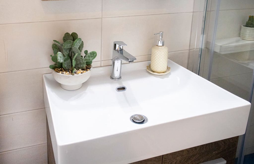 Λευκός νιπτήρας σε ανακαίνιση μπάνιου στην Καλλιθέα με χρωμέ μπαταρία και minimal σχεδιασμό