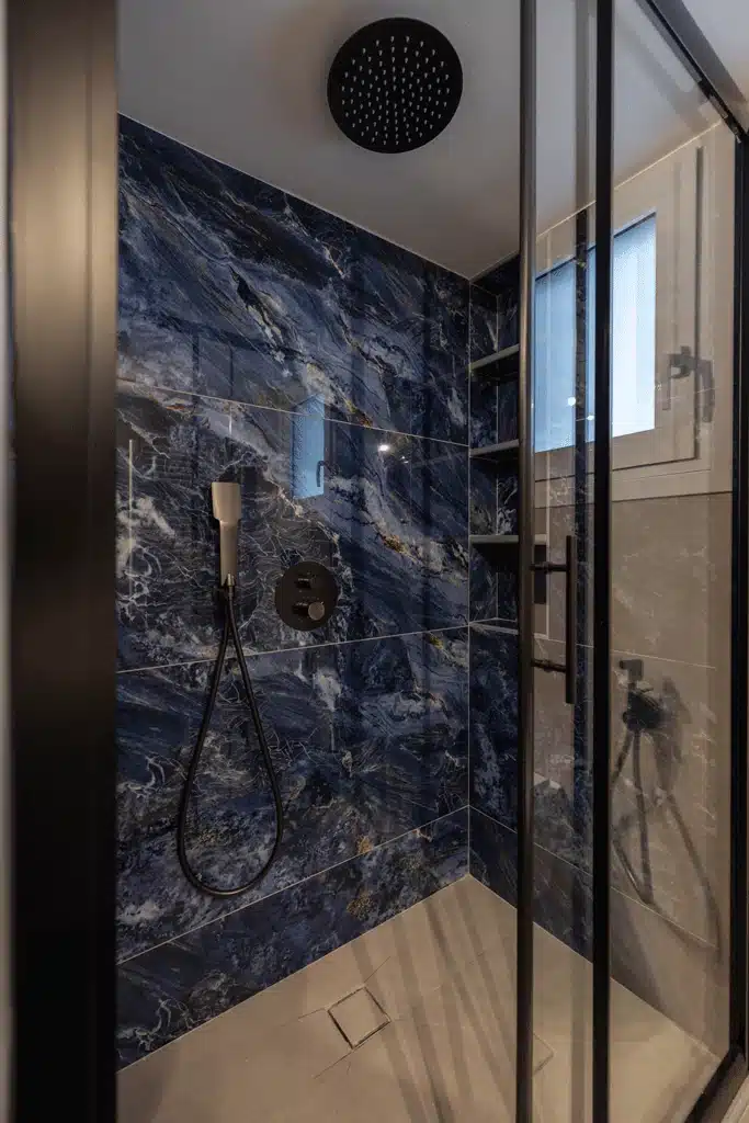 Ντουζιέρα μπάνιου με γυάλινη καμπίνα, μπλε marble πλακάκια τοίχου και μαύρη στήλη ντους οροφής