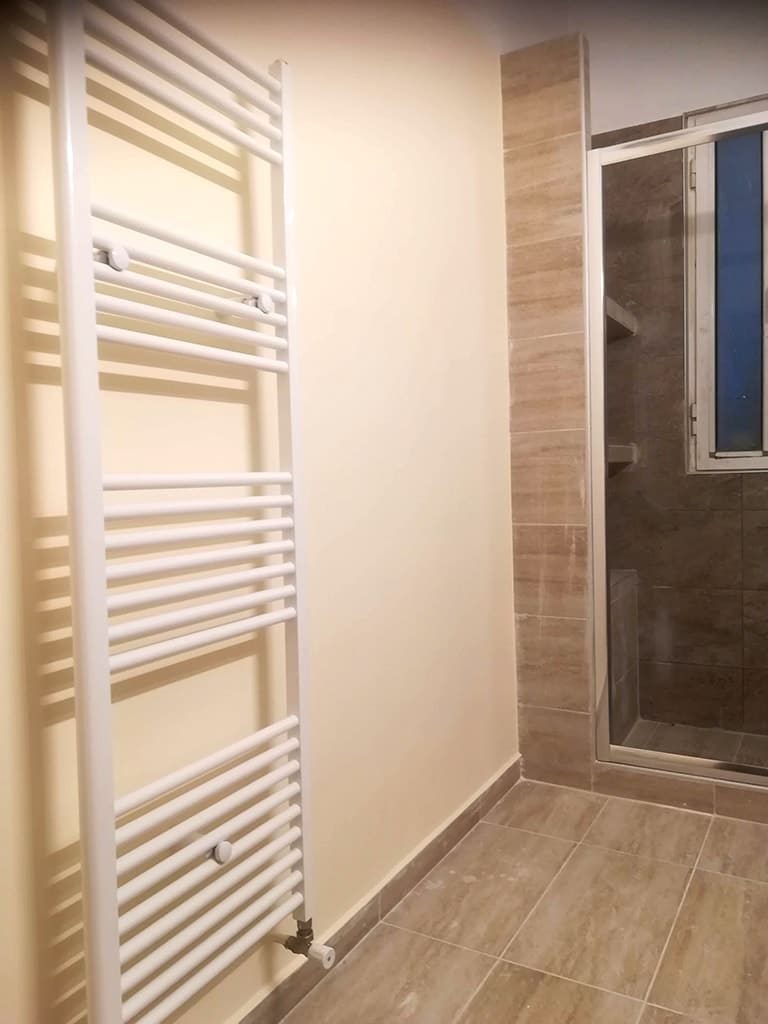 θερμαντικό σώμα μπάνιου πετσετοκρεμάστρα δίπλα σε καμπίνα ντουζιέρας σε ανακαινισμένο μπάνιο στον Άγιο Στέφανο
