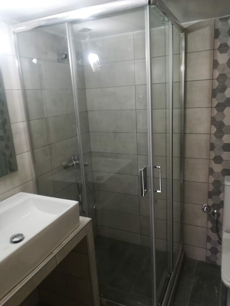 χτιστή ντουζιέρα με γωνιακή γυάλινη καμπίνα σε ανακαίνιση μπάνιου με γκρι πλακάκια